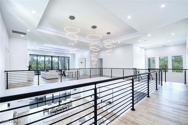 hallway with visible vents, a healthy amount of sunlight, a raised ceiling, and wood finished floors