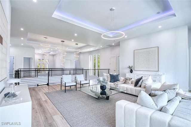 living room with a raised ceiling, recessed lighting, and light wood-type flooring