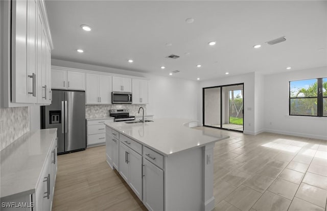 kitchen featuring sink, white cabinetry, stainless steel appliances, a kitchen island with sink, and backsplash