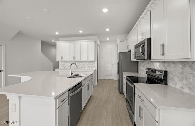 kitchen with tasteful backsplash, sink, white cabinets, stainless steel appliances, and a center island with sink