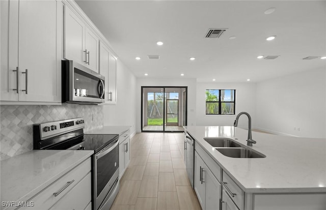 kitchen with sink, tasteful backsplash, appliances with stainless steel finishes, an island with sink, and white cabinets