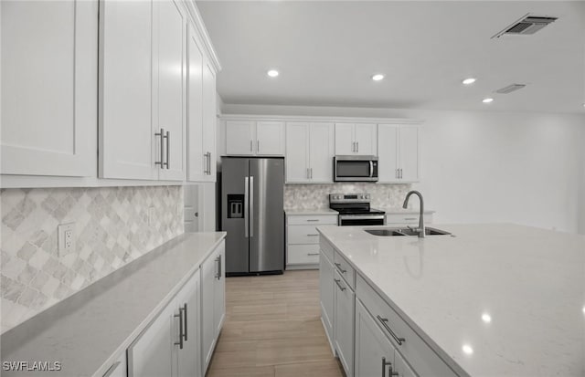 kitchen with sink, white cabinetry, tasteful backsplash, appliances with stainless steel finishes, and light stone countertops