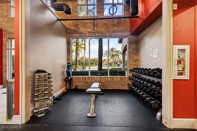 exercise room with a high ceiling and brick wall