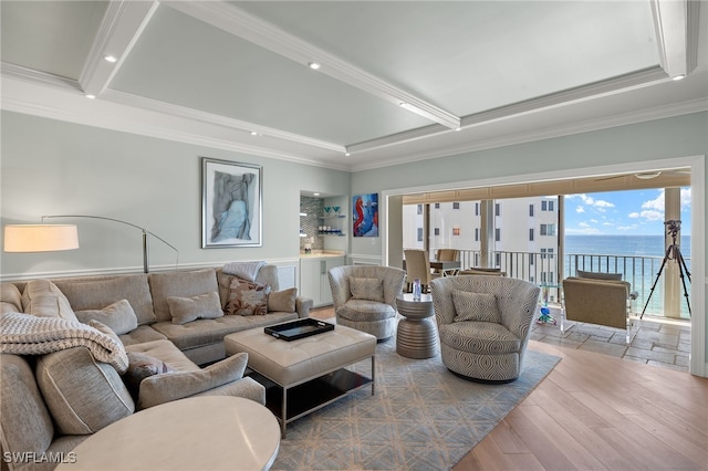 living room featuring a raised ceiling, ornamental molding, a water view, and light wood-type flooring