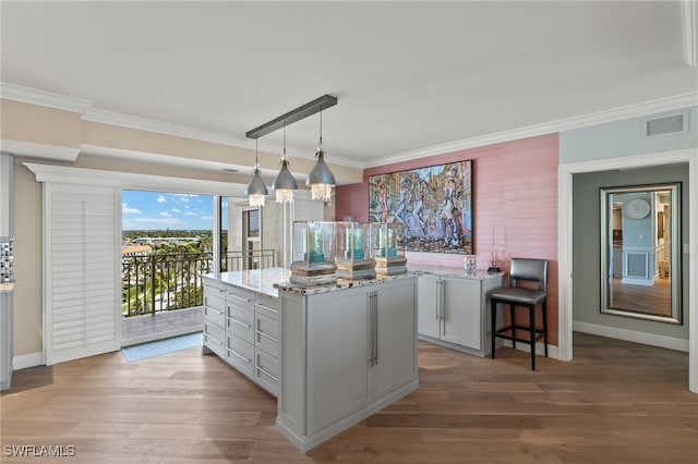 kitchen with light stone counters, decorative light fixtures, a center island, ornamental molding, and hardwood / wood-style floors