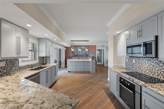 kitchen with pendant lighting, crown molding, appliances with stainless steel finishes, light stone countertops, and light hardwood / wood-style floors