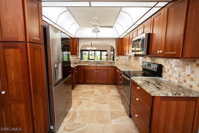 kitchen with sink, light stone counters, appliances with stainless steel finishes, a notable chandelier, and decorative backsplash