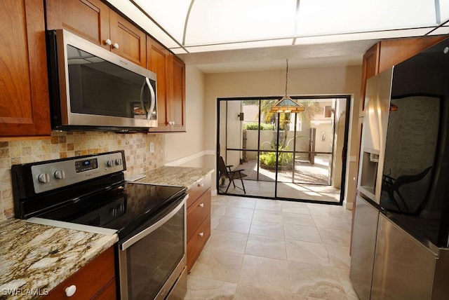 kitchen featuring light tile patterned flooring, light stone counters, pendant lighting, stainless steel appliances, and backsplash