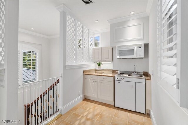 kitchen featuring light tile patterned floors, visible vents, white microwave, ornamental molding, and a sink