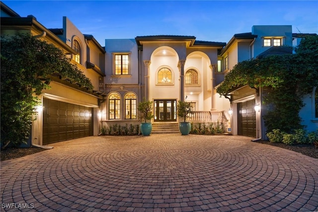 mediterranean / spanish house with a garage, stucco siding, curved driveway, and french doors