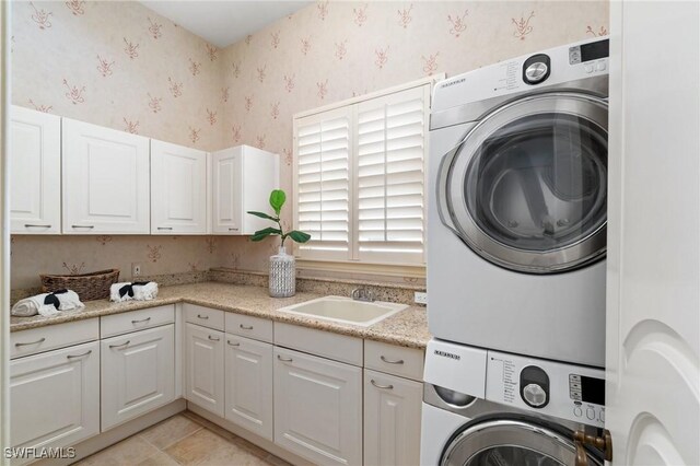 clothes washing area featuring wallpapered walls, cabinet space, a sink, and stacked washer / drying machine