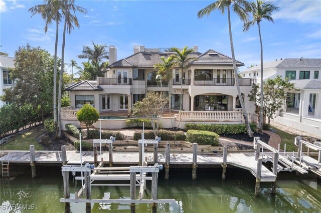 dock area featuring a water view, boat lift, a balcony, and an outdoor pool