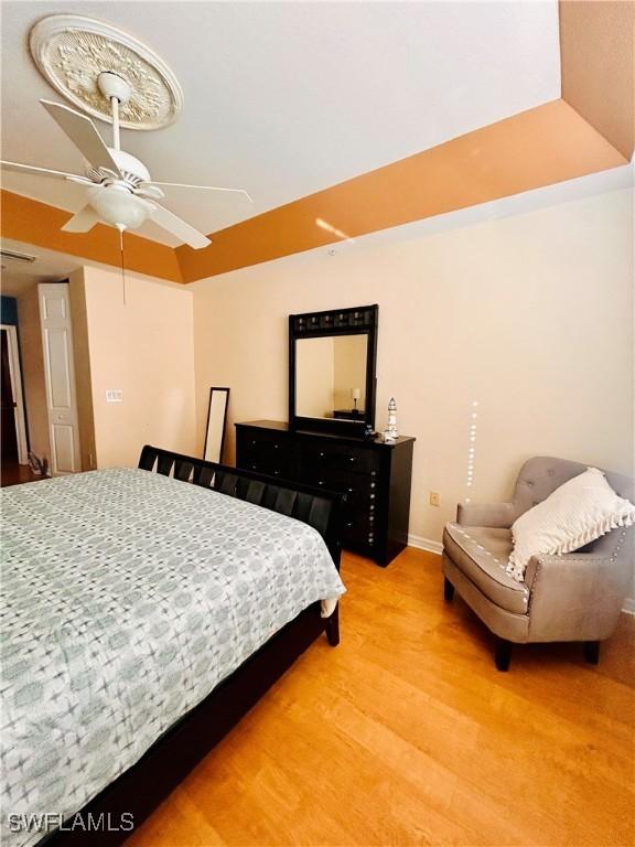 bedroom featuring ceiling fan, wood-type flooring, and a raised ceiling