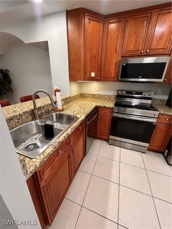 kitchen with stainless steel appliances, light tile patterned flooring, a sink, and light stone countertops