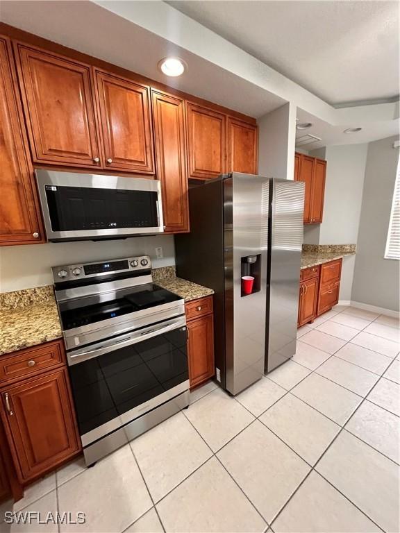 kitchen featuring brown cabinets, light tile patterned floors, recessed lighting, appliances with stainless steel finishes, and light stone countertops