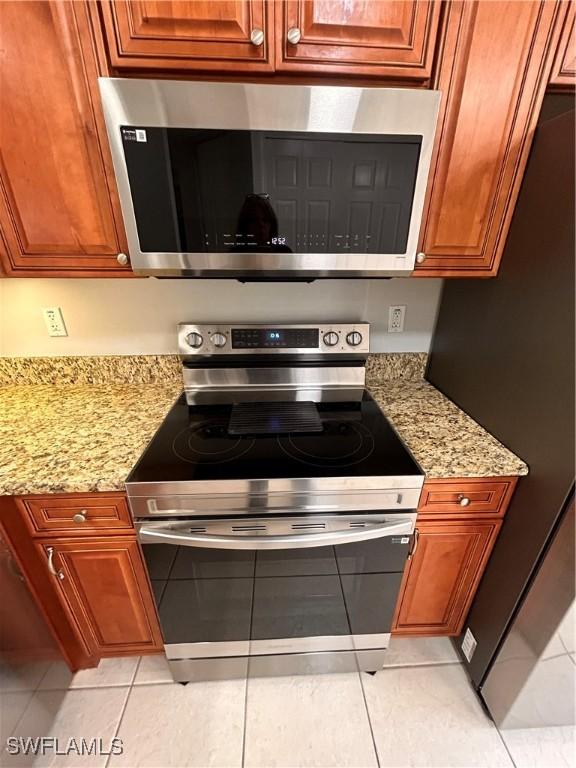 kitchen with light tile patterned floors, appliances with stainless steel finishes, brown cabinetry, and light stone counters