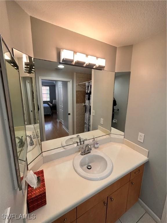 bathroom featuring vanity, baseboards, a textured ceiling, and ensuite bathroom