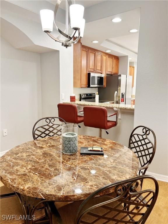 dining room featuring baseboards, light wood-style flooring, an inviting chandelier, a tray ceiling, and recessed lighting