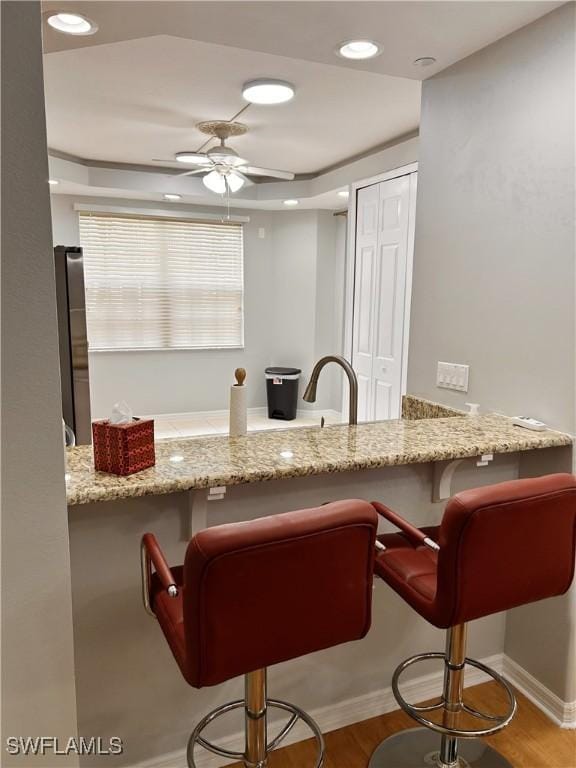 kitchen with light stone counters, a peninsula, a kitchen bar, and a ceiling fan