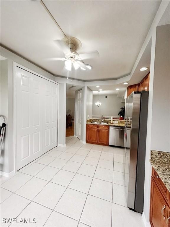 kitchen featuring light tile patterned floors, brown cabinetry, ceiling fan, appliances with stainless steel finishes, and light stone countertops