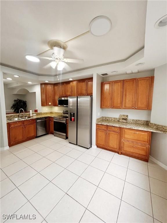 kitchen with light stone counters, stainless steel appliances, a sink, baseboards, and brown cabinetry