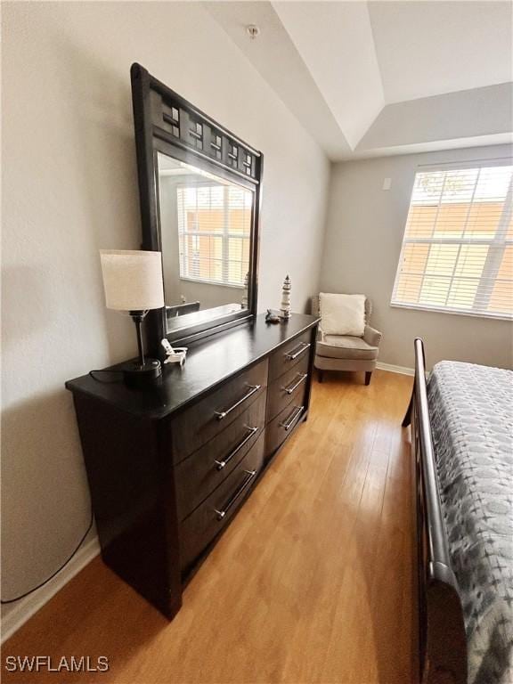 bedroom featuring light wood-style floors, a raised ceiling, and baseboards