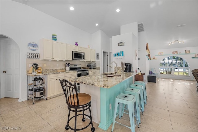 kitchen featuring sink, light stone counters, light tile patterned floors, appliances with stainless steel finishes, and a kitchen breakfast bar