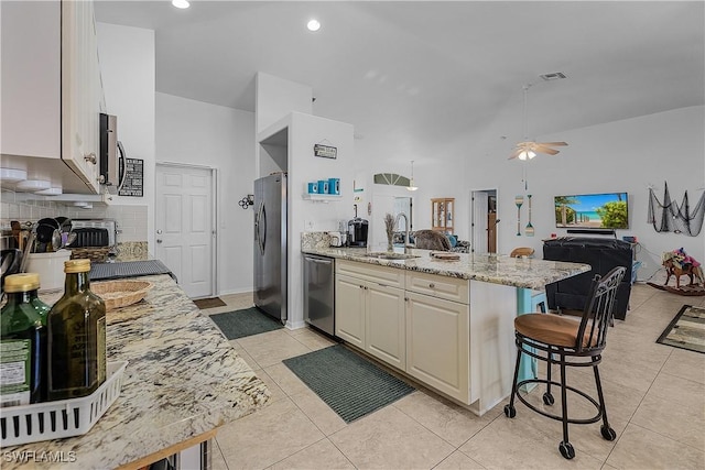 kitchen with sink, stainless steel appliances, light stone counters, a kitchen bar, and decorative backsplash
