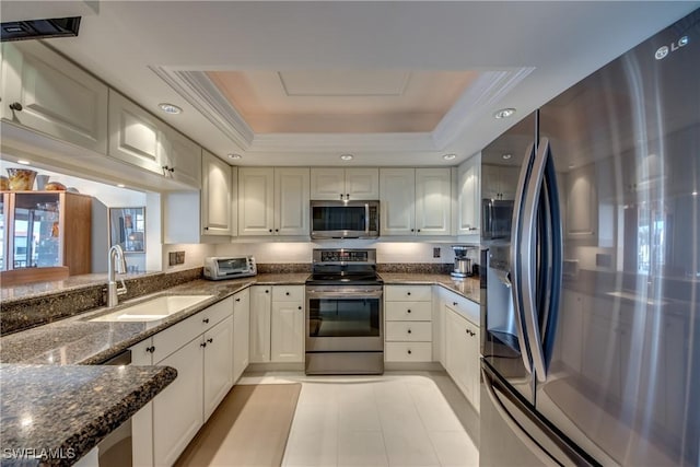 kitchen with sink, white cabinetry, stainless steel appliances, a tray ceiling, and dark stone counters