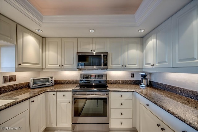 kitchen featuring appliances with stainless steel finishes, a tray ceiling, dark stone counters, and white cabinets