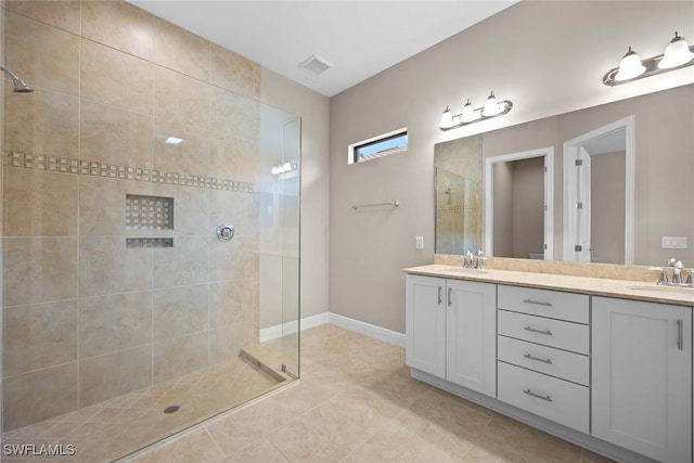 bathroom featuring double vanity, visible vents, a sink, tiled shower, and baseboards