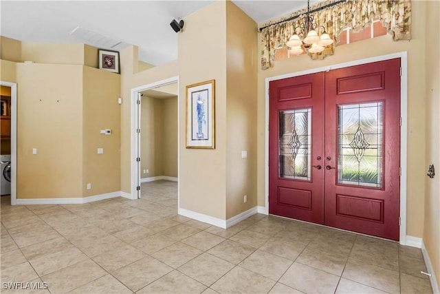 tiled foyer entrance with french doors, washer / clothes dryer, and a notable chandelier