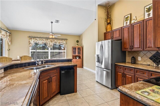 kitchen featuring vaulted ceiling, light tile patterned flooring, tasteful backsplash, sink, and stainless steel fridge with ice dispenser