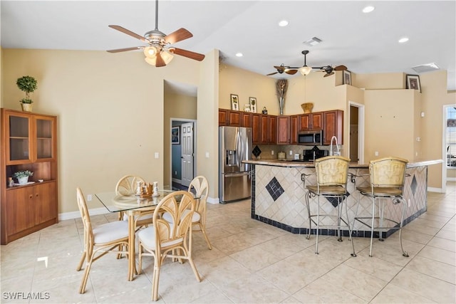 kitchen with light tile patterned floors, ceiling fan, appliances with stainless steel finishes, backsplash, and a kitchen bar