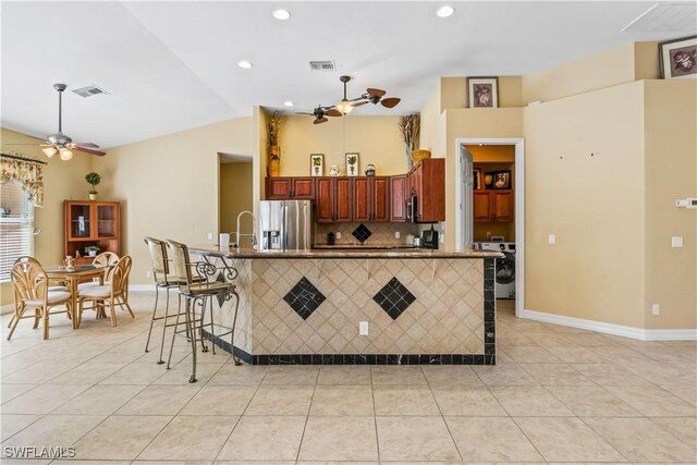 kitchen with light tile patterned floors, stainless steel fridge, a breakfast bar area, and ceiling fan