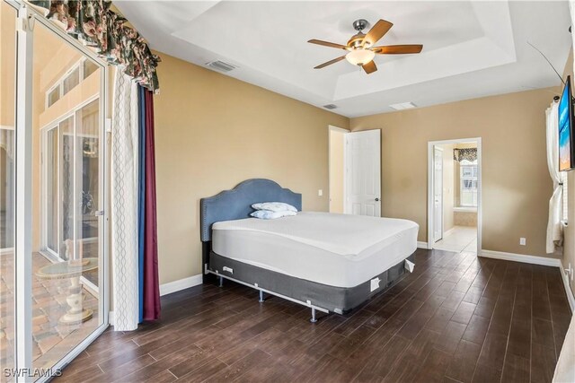 bedroom with dark hardwood / wood-style floors, ceiling fan, ensuite bathroom, and a tray ceiling