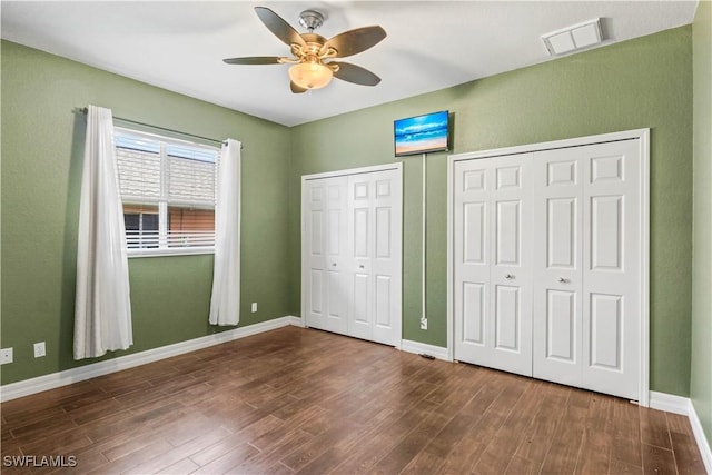 unfurnished bedroom featuring multiple closets, dark hardwood / wood-style floors, and ceiling fan