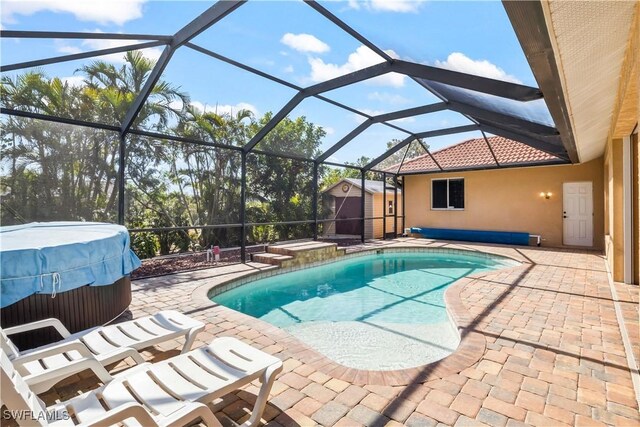 view of pool with a lanai, a hot tub, a patio, and a storage unit