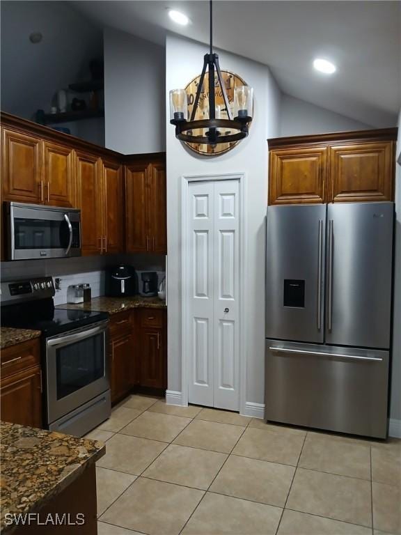 kitchen featuring light tile patterned flooring, appliances with stainless steel finishes, lofted ceiling, dark stone countertops, and an inviting chandelier