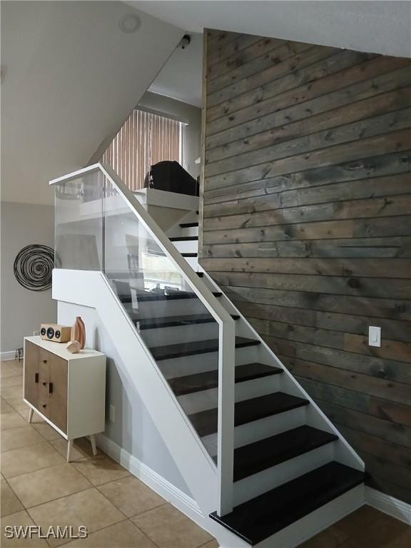 stairs with vaulted ceiling, tile patterned flooring, and wood walls