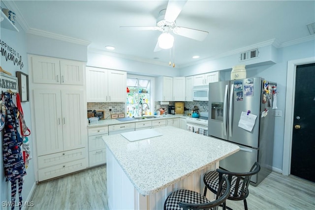 kitchen with a breakfast bar, white cabinetry, light stone counters, a center island, and white appliances