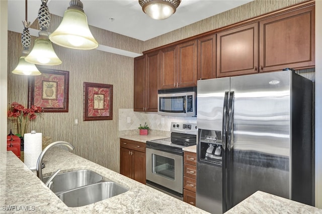 kitchen featuring hanging light fixtures, appliances with stainless steel finishes, sink, and light stone counters