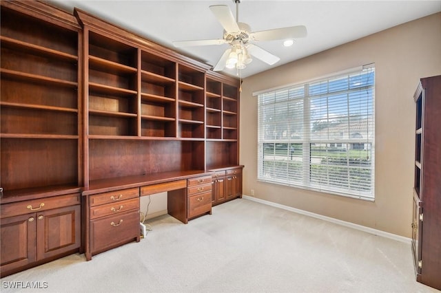 office with built in desk, light colored carpet, and ceiling fan