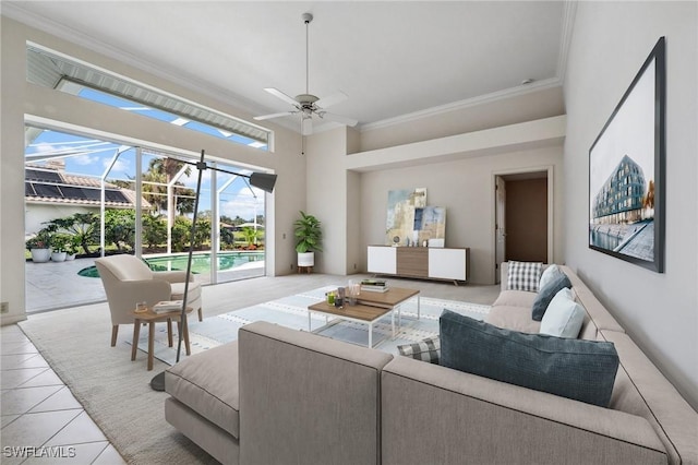 living area featuring light tile patterned floors, a ceiling fan, a towering ceiling, a sunroom, and crown molding