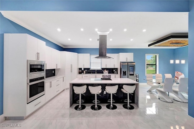 kitchen with appliances with stainless steel finishes, a breakfast bar, island range hood, white cabinetry, and a center island with sink