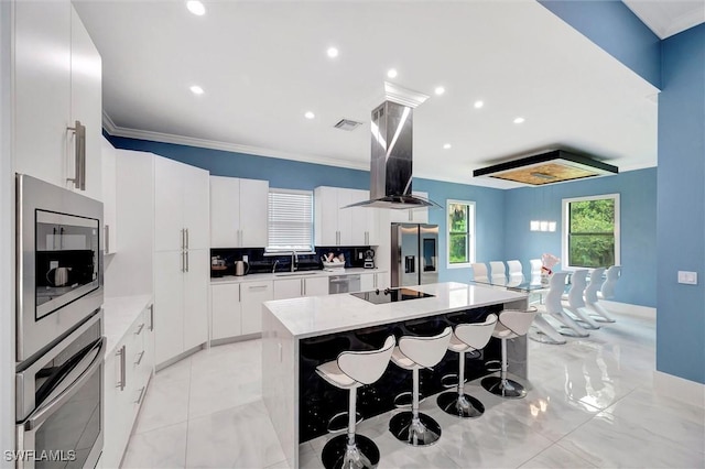 kitchen with a kitchen island, a breakfast bar, white cabinets, island exhaust hood, and stainless steel appliances