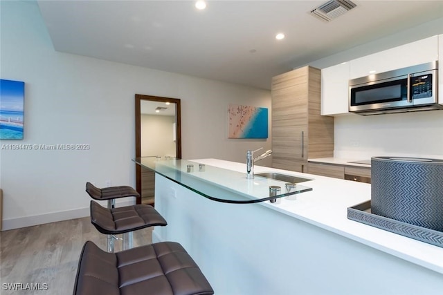 kitchen featuring sink, light hardwood / wood-style flooring, stovetop, white cabinetry, and a kitchen breakfast bar