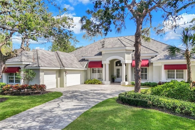 view of front facade with a front lawn, decorative driveway, a garage, and stucco siding