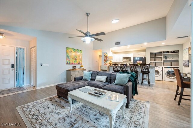 living room with ceiling fan, washer and clothes dryer, high vaulted ceiling, and light hardwood / wood-style flooring