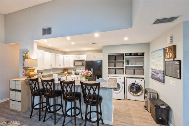 kitchen with a breakfast bar, black appliances, independent washer and dryer, light stone countertops, and white cabinets